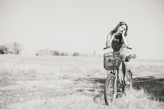 Young pinup woman cycling in fields under summer sky copy space image
