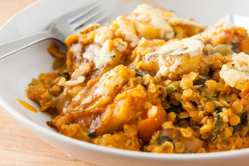 Close-up view of a lentil and vegetable hotpot with a cheesy potato topping in a white china bowl