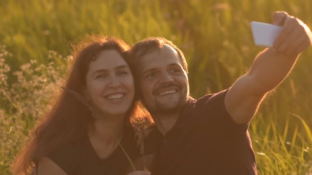 Happy romantic couple walking in the Park at sunset and taking a selfie. A young man after a selfie kissing his girlfriend.