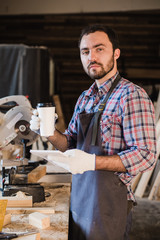 Carpenter taking a coffee break holding notebook in front of circular saw at his workshop