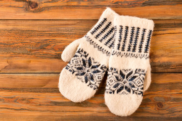 White mittens with ornament on wooden background.