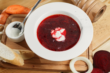 Ukrainian and Russian traditional beetroot soup - borscht in clay pot with sour cream, spice, garlic, pepper, dried herbs  bread on dark wooden background, healthy food
