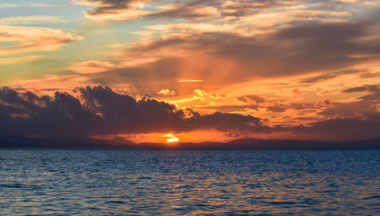 Sunset on the blue sea with clouds. The sun between clouds, .