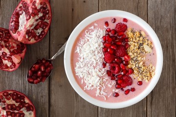 Smoothie bowl with pomegranates, raspberries, coconut and granola, overhead scene on rustic wood