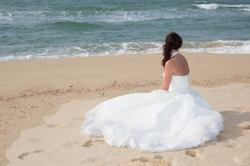 Fototapeta na wymiar Bride sitting along sea coast in the wedding dress