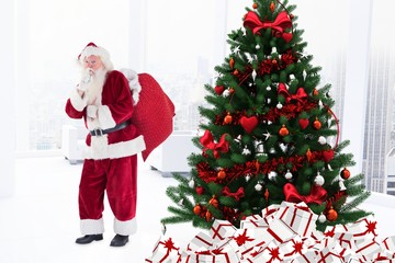 Santa claus with finger on lips standing near christmas tree