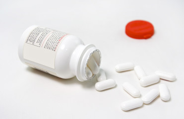 Overturned plastic medicine bottle with white capsules spilling from the mouth of the bottle. Back label of bottle is visible. Horizontal.