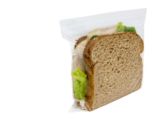 Basic turkey sandwich with lettuce on brown wheat bread in plastic baggie. Front and side view. Horizontal.