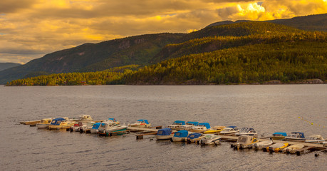 Motor speed fishing boats tied with ropes to lake pier in Norway during sunset, Mountains fishing lake with wooden jetty for motorboats, tied to pier. Amazing north mountains lake sunset landscape