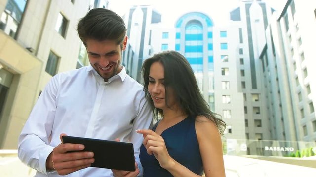 Beautiful businesswoman and her handsome colleague using tablet in the street.