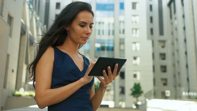 Young beautiful serious business lady using tablet on the street.