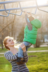 Mom assists son to the horizontal bars.