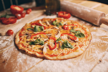 Top wiev pizza lies on textural woden table near A wooden cutting board which there are all the ingredients chopped.