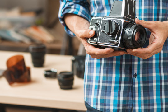 Old professional medium format photo camera close-up. Unrecognizable photographer holding film camera, blurred negatives on background, free space for text