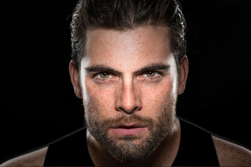 Handsome male athlete body builder with facial hair and intense eyes on isolated black background