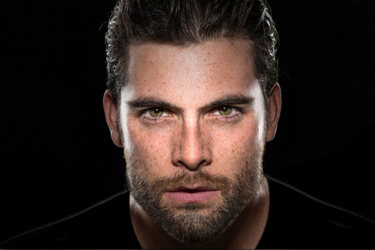 Handsome male model with masculine facial hair and intense eyes on isolated black background 