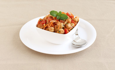 Indian vegetarian food channa chat, also known as chickpea or garbanzo curry, is eaten as a snack or is used as a side dish, in a bowl on a plate with a spoon.