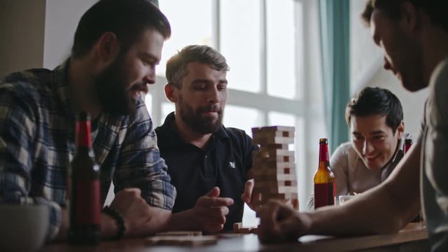 Man carefully taking jenga wooden block from bottom of tower while playing with friends at party