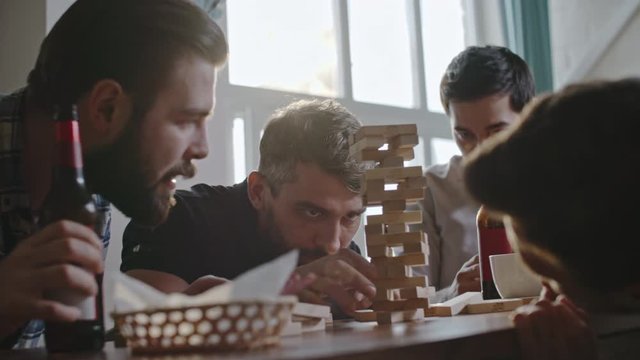 Group of male friends looking at jenga tower picking strategy but then making it fall down by accident