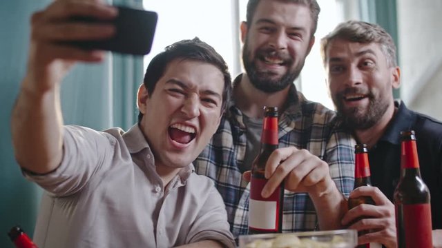 Tipsy male friends with bottles of beer taking selfie and laughing