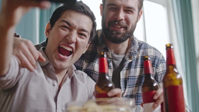 Asian man laughing and taking selfie with posing bearded friends with beer