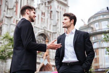 Two cheerful young businessmen standing and talking