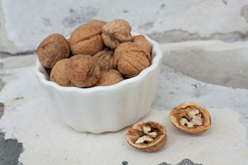 walnuts in their shells in a white bowl on a concrete background