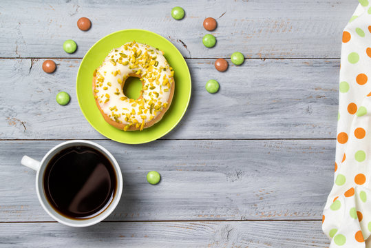 Cup of coffee, pistachios donut on a plate and candies, wooden background, top view