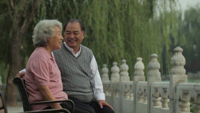 MS Elderly couple talking and laughing, sitting on park bench /Beijing, China
