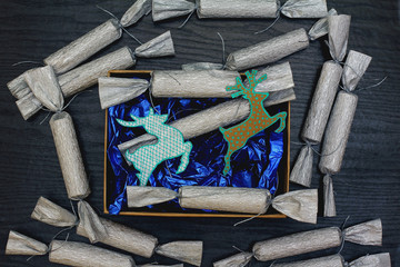 Сandy in a silver wrapper on a black wood background. Blue wrapping paper and kraft box. Christmas decorations in the form of a deer. Top view, flat lay