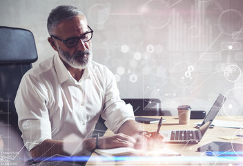 Concept of digital screen with global virtual icon,diagram, graph interface.Adult successful businessman wearing a classic glasses and working at the wood table in modern loft studio.Horizontal,flare.