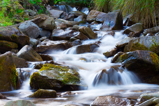 Mountain stream(creek) in the stones and green grass banks in mountain forest. Crystal clear water - rare condition of modern enviroment. Long exposure.