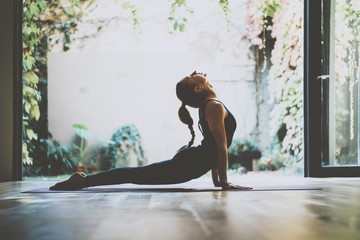 Portrait of gorgeous young woman practicing yoga indoor. Beautiful girl practice cobra asana in class.Calmness and relax, female happiness.Horizontal, blurred background.