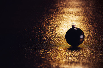 Dark Christmas ball laying on a festive golden fabric in a streak of light