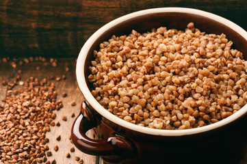 Boiled buckwheat porridge in ceramic pot on wooden background.