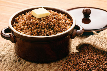 Boiled buckwheat porridge in ceramic pot on wooden background.