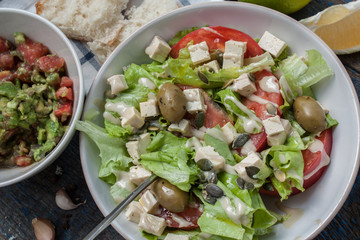Guacamole - latin american sauce and ingredients (avocado, tomatoes, onion, lemon, garlic, lime) and green salad with tofuonblue wooden background. Love for a healthy raw food concept