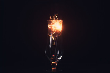 Sparkler on a black background, sparks fly in different directions, elegant glass,