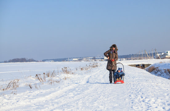 Mother and her little son on sled on cold winter day 
