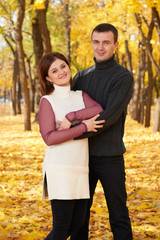 Fototapeta premium romantic people, happy adult couple embrace in autumn city park, trees with yellow leaves, bright sun and happy emotions, tenderness and feelings