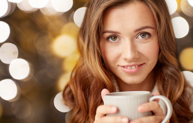 close up of happy woman with tea cup over lights