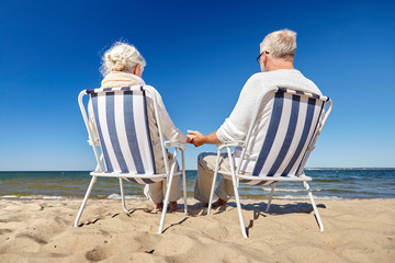 senior couple sitting on chairs at summer beach