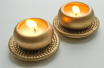 Fototapeta na wymiar Two burning decorative candles in gold color on a light background