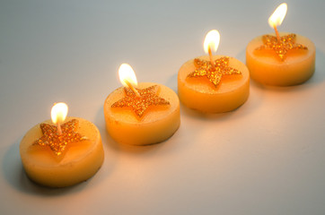 Four burning decorative candles with star pattern on a light background
