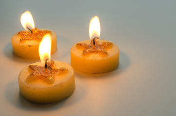 Fototapeta na wymiar Three burning decorative candles with star pattern on a light background 
