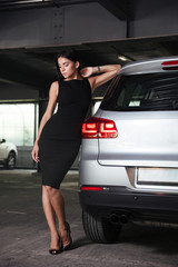 Beautiful young woman in black dress standing near her car