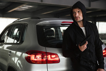 Criminal man with gun standing near car on parking