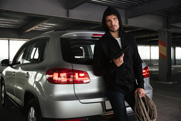 Man holding gun and rope near the car on parking