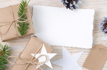 Christmas background. Holiday decorations: gifts, cones, stars on light wooden table. Paper with space for writing.  Top view.