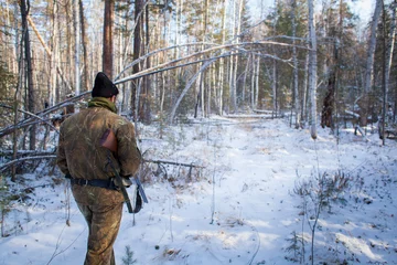 Schilderijen op glas a hunter in the winter woods with a gun in camouflage clothing. © nikstar_2012
